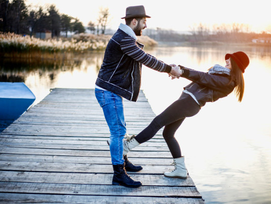 A couple stands on a dock, hand in hand