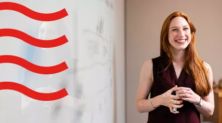 lady with red hair and black top smiling next to whiteboard