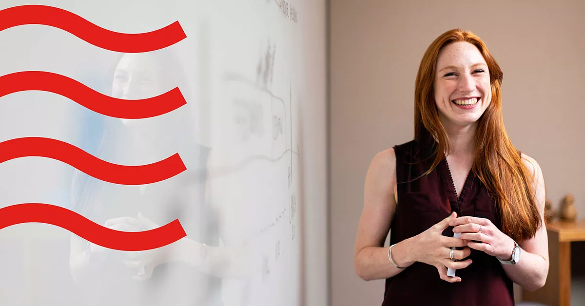 lady with red hair and black top smiling next to whiteboard