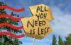 Cardboard protest sign reading ‘All you need is less’ held up outdoors.