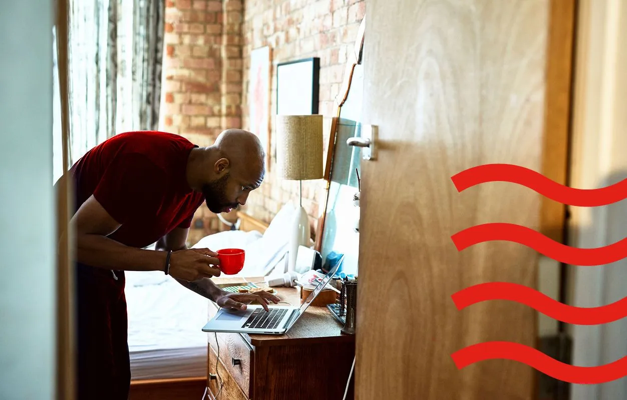 A man at home checking his laptop while drinking coffee